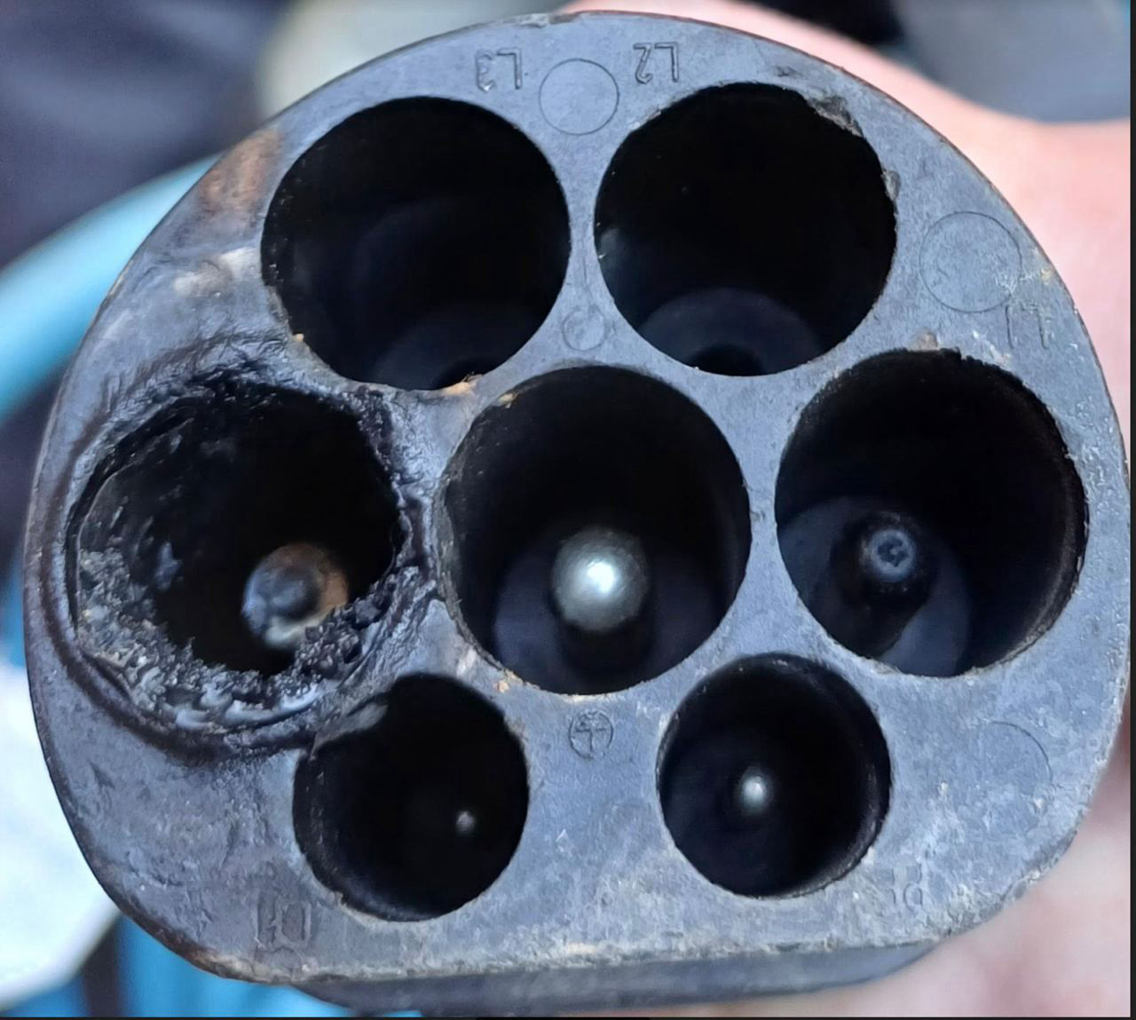 Face of a Type 2 EV charging connector with one contact burnt out and the surrounding plastic melted and charred